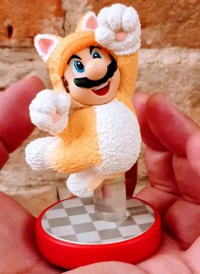 A hand holding a model of Mario, dressed in a cat costume, jumping in the air.