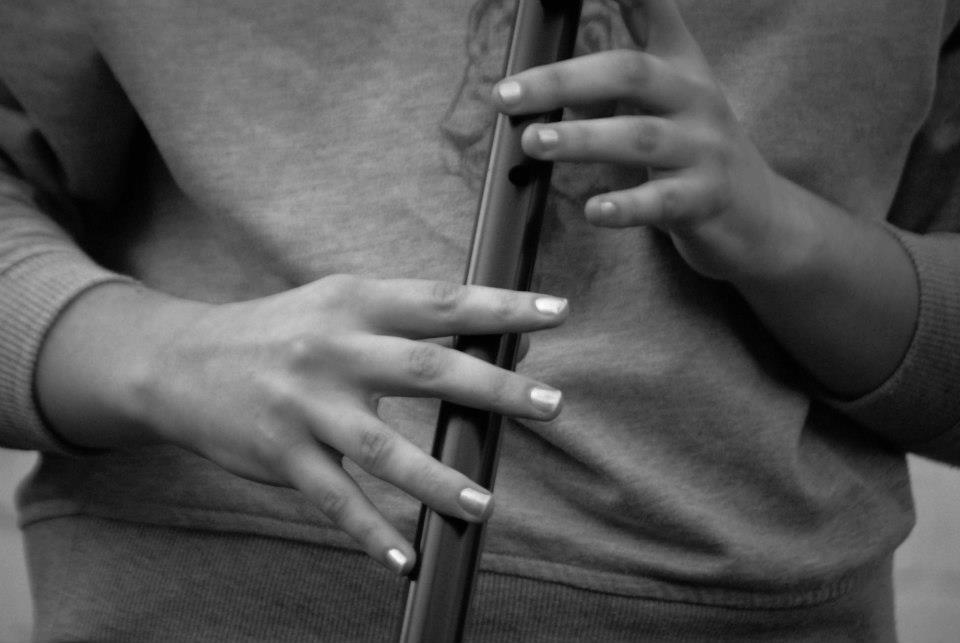 Hands playing a black low D whistle.